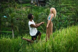 A man on one knee proposing to a woman in the woods