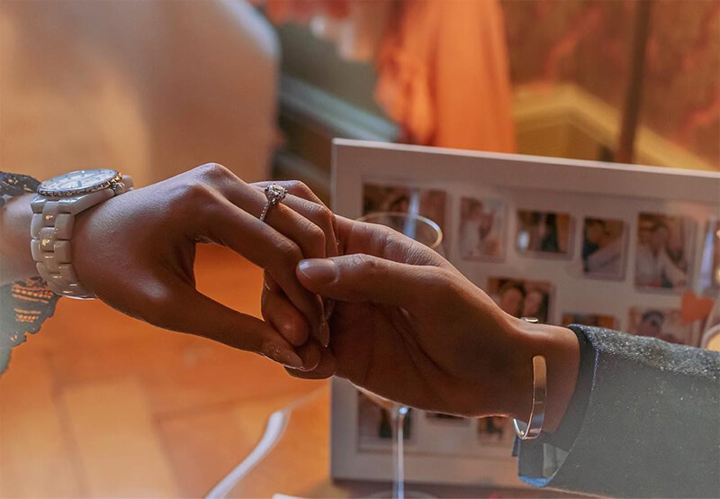 A couple holding hands with rings right after wedding proposal in an indoor setup.